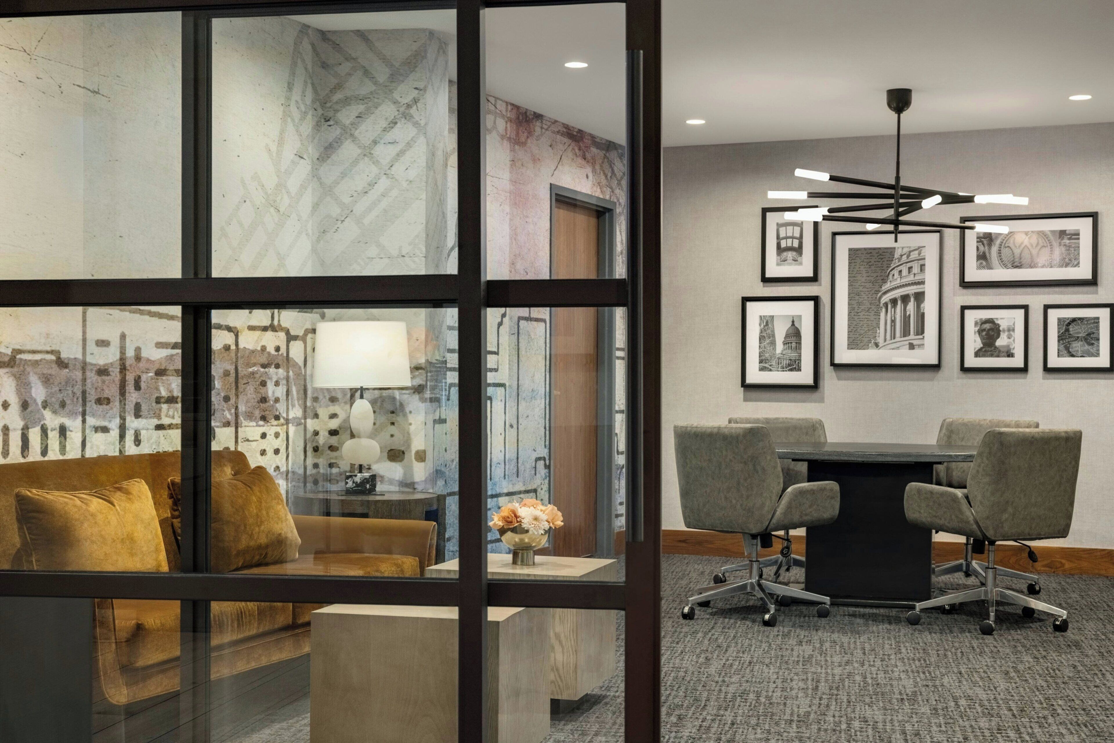 A modern office space with a glass partition, a sofa, a desk with a lamp, and a conference table with chairs.