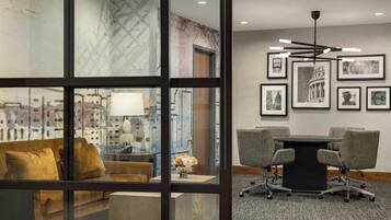 A modern office space with a glass partition, a sofa, a desk with a lamp, and a conference table with chairs.
