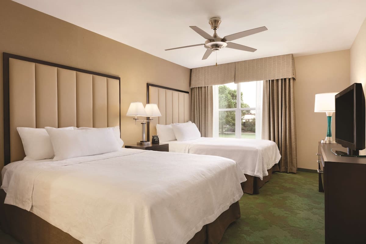 Une chambre d’hôtel avec deux lits, un ventilateur de plafond, une télévision et une fenêtre avec des rideaux.