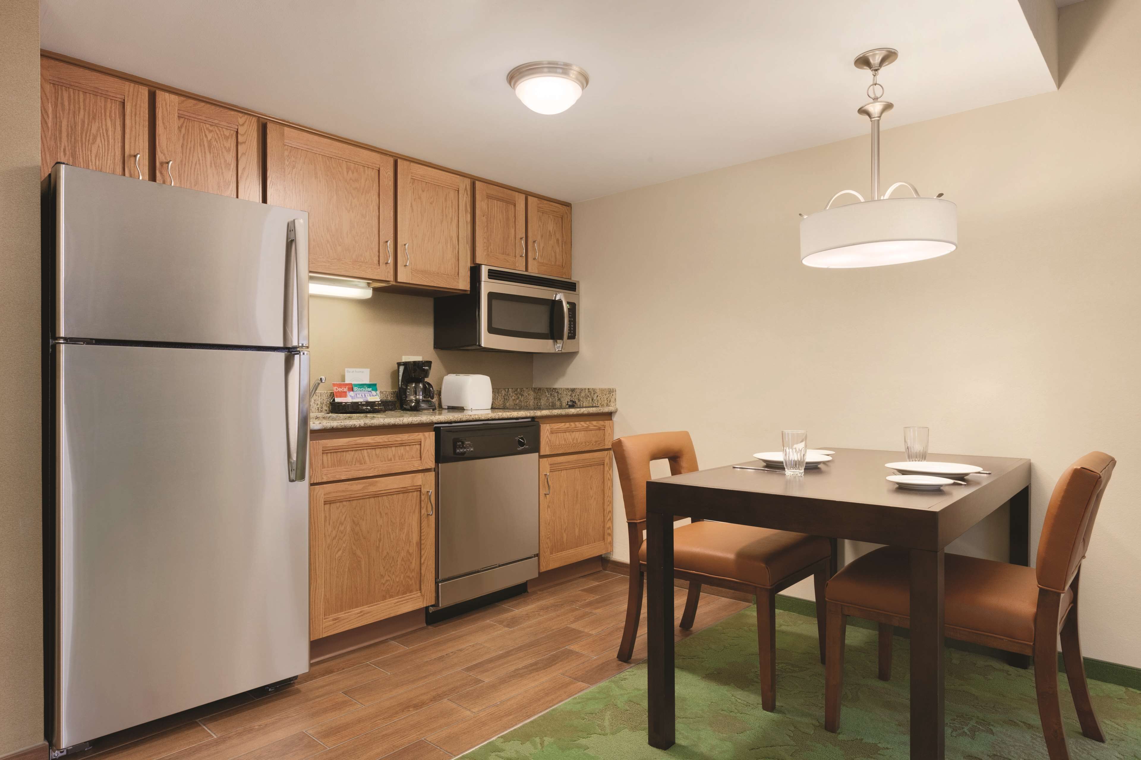 A kitchen with wooden cabinets, stainless steel appliances, a dining table with chairs, and a hanging light fixture.