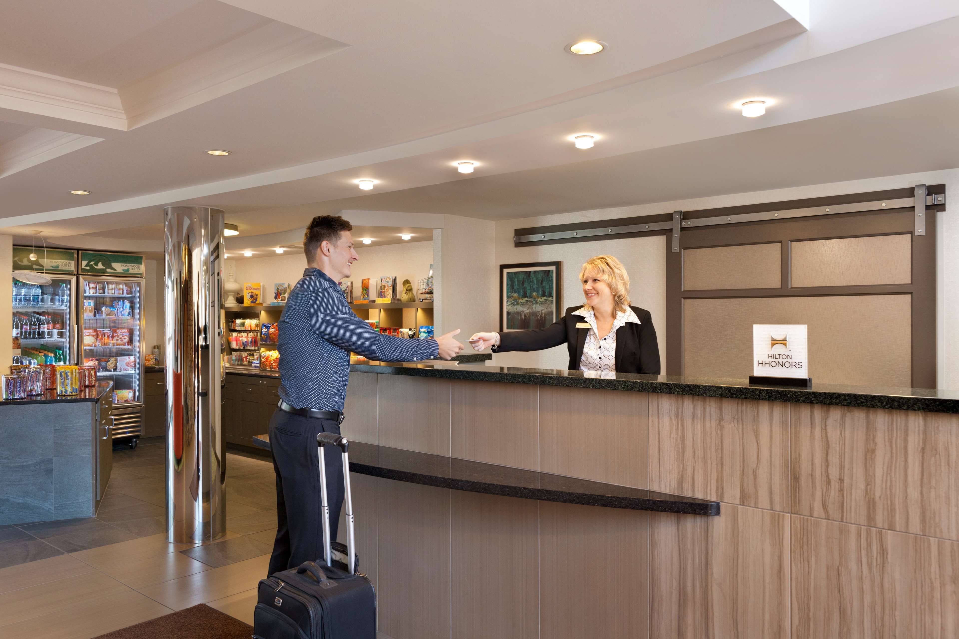 Ein Hotel-Rezeptionsbereich mit Empfangstheke, einer mit Getränken gefüllten Kühlbox und einem Schild mit dem Hotelnamen.