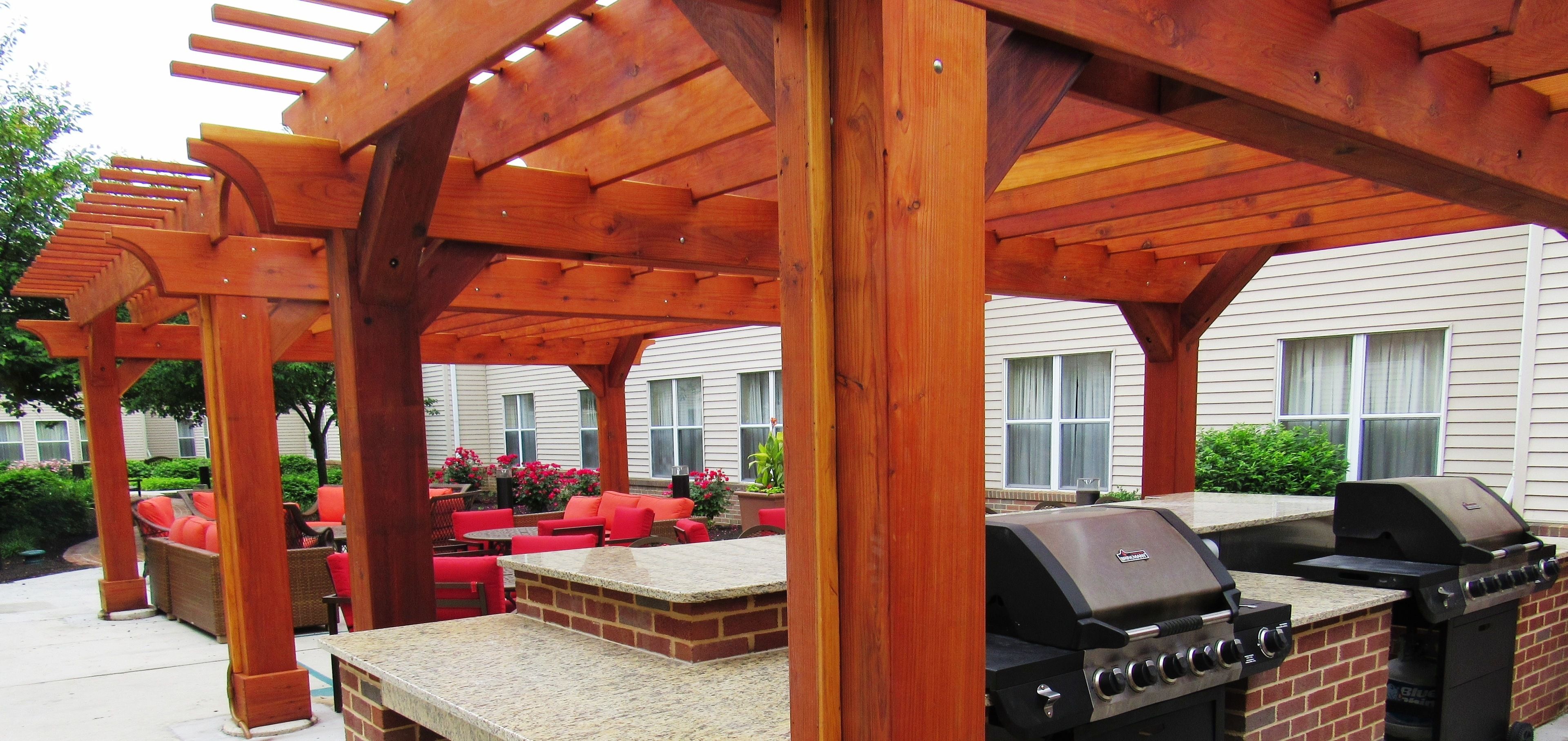 An outdoor patio with a wooden pergola, red seating, and a built-in grill.