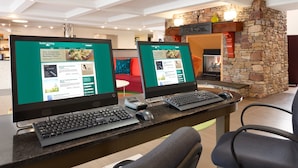 A hotel reception area with two computer monitors displaying the 'Suite Living' website, a stone fireplace, and a modern interior design. - Homewood Suites by Hilton Harrisburg-West Hershey Area (Mechanicsburg)