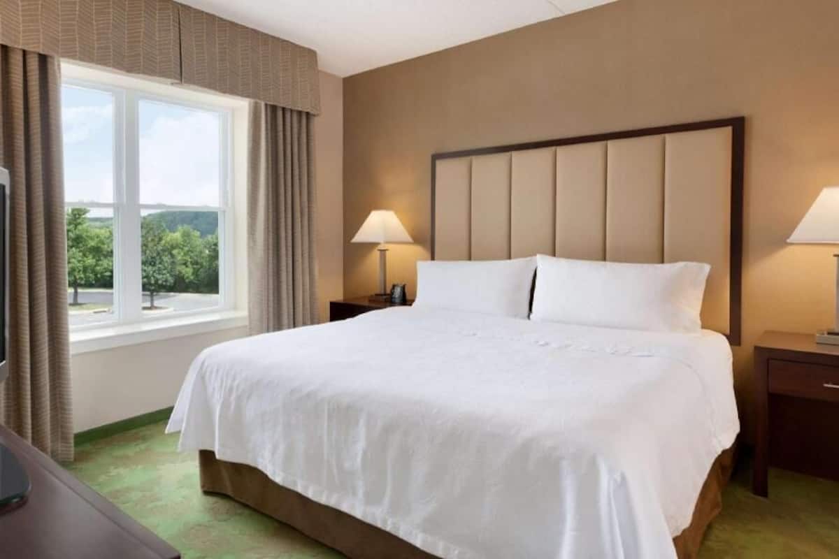 Une chambre d’hôtel avec un grand lit, deux tables de chevet, une télévision et une fenêtre avec des rideaux.