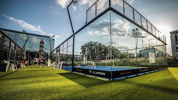 Instalación deportiva con cerramiento de vidrio, césped artificial y marca visible.