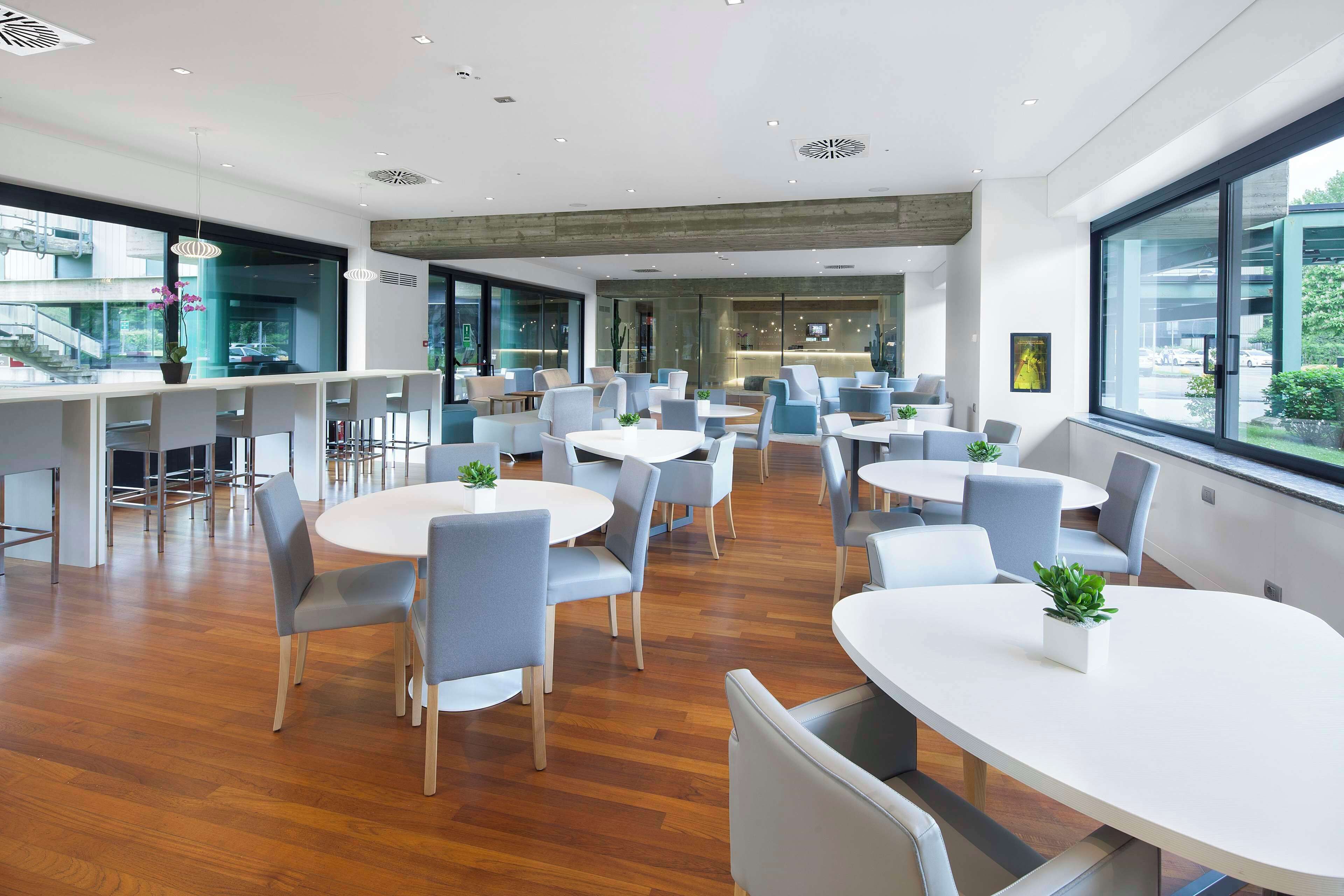 A modern dining area with round tables and chairs, large windows, and a view of the city.