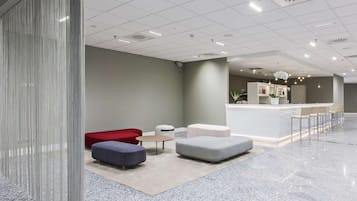 A modern lobby with a reception desk, seating area, and a decorative plant.