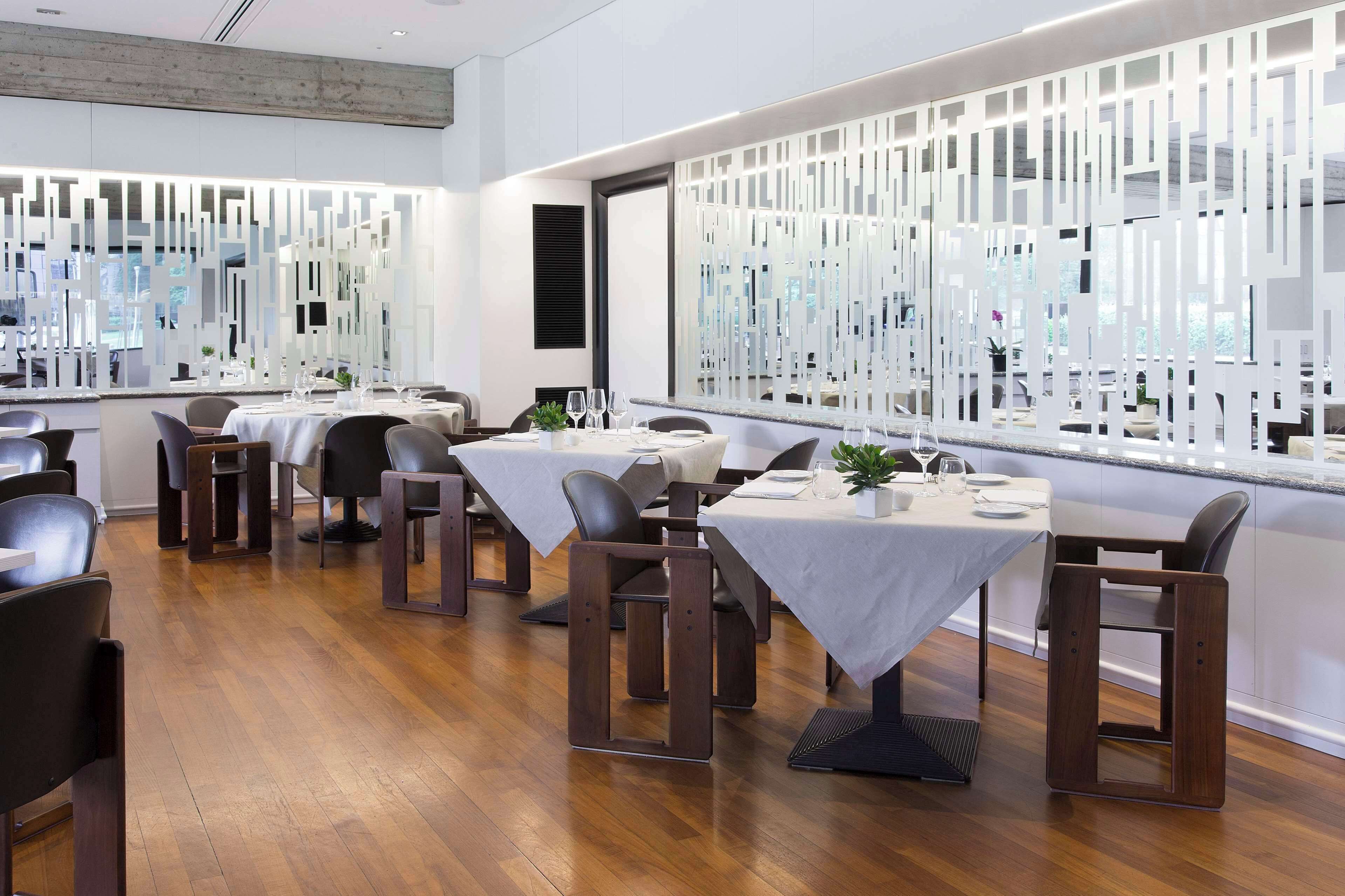 A modern restaurant with wooden flooring, white tables, and black chairs.