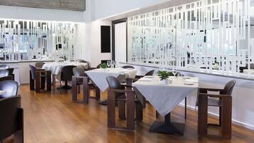 Een modern restaurant met houten vloeren, witte tafels en zwarte stoelen.
