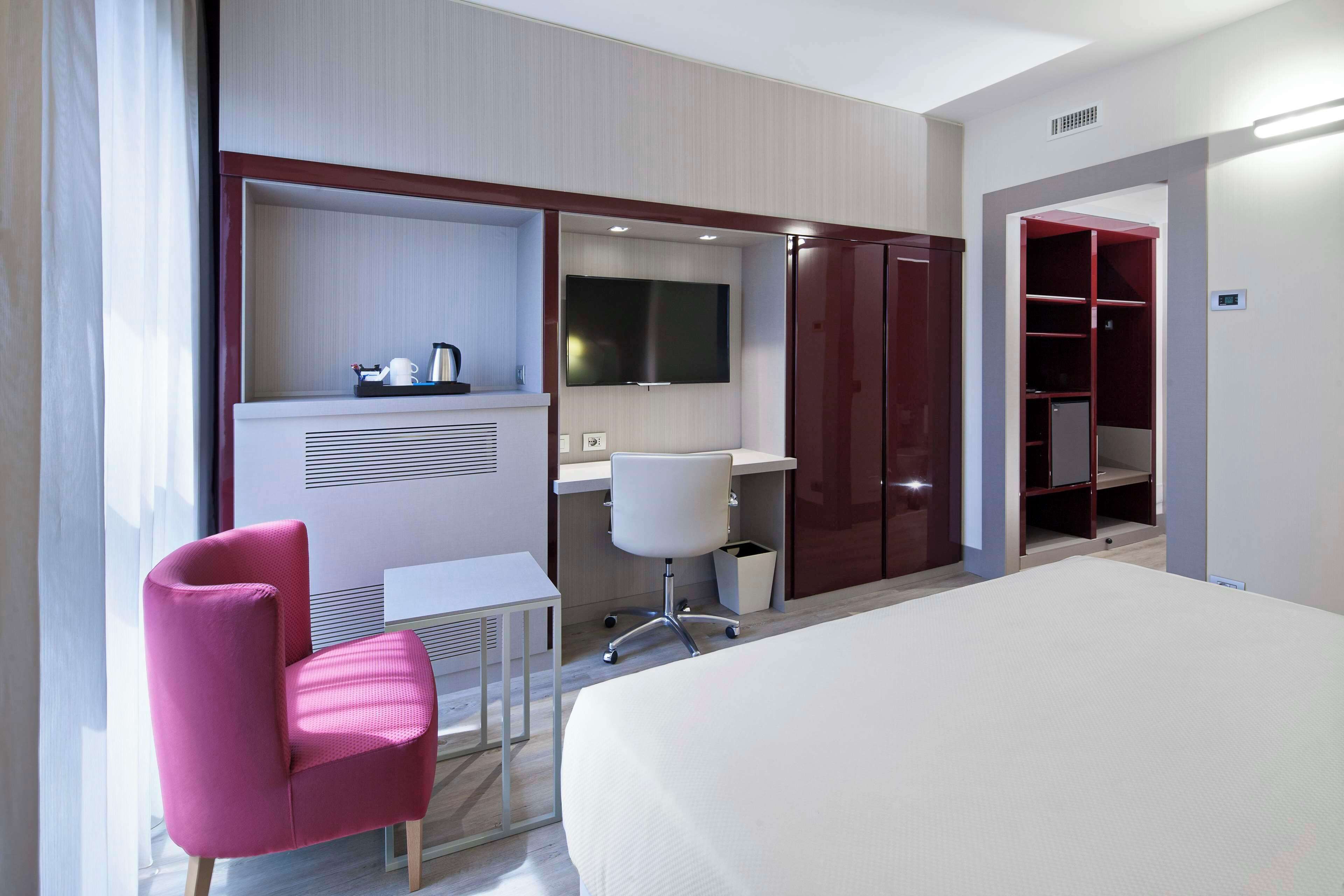 Ein Hotelzimmer mit Bett, Schreibtisch, Stuhl, Fernseher und Kleiderschrank.