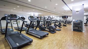Un gimnasio con cintas de correr, máquinas de pesas y un espejo grande.