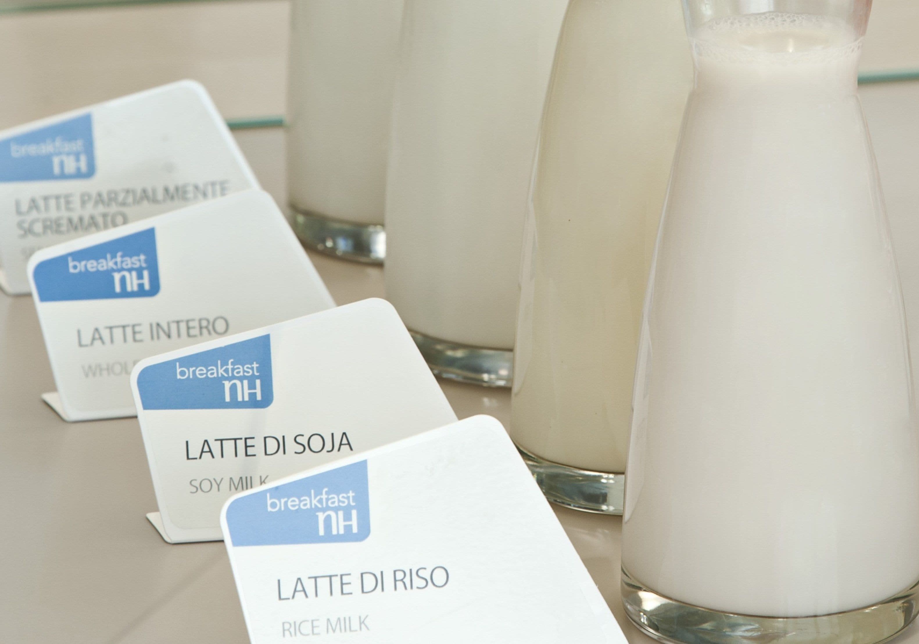 Een rij melkpakken met verschillende soorten melk, waaronder sojamelk en rijstmelk, naast een glas melk.