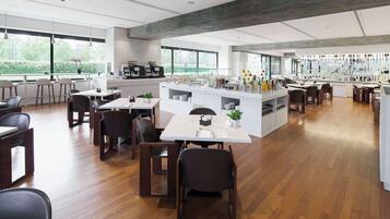 Ein modernes Restaurant mit Holzboden, weißen Tischen und schwarzen Stühlen. Es gibt eine Bar mit einer Theke und verschiedenen Flaschen.