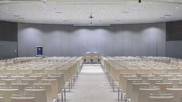 Un amplio salón de conferencias con filas de sillas, un atril y una pantalla de proyección.