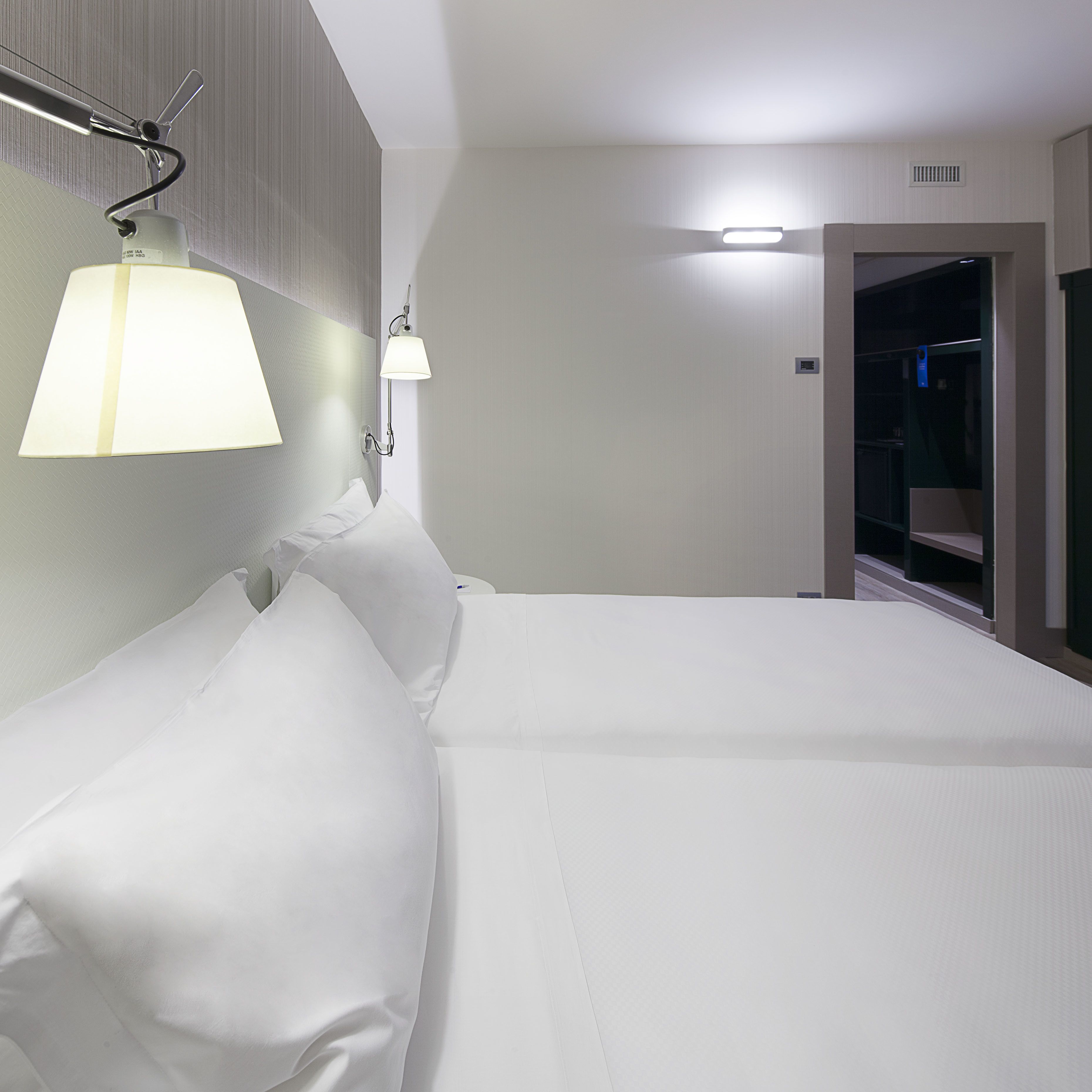 Una habitación de hotel con una cama grande, una lámpara fijada a la pared y una puerta que da al baño.
