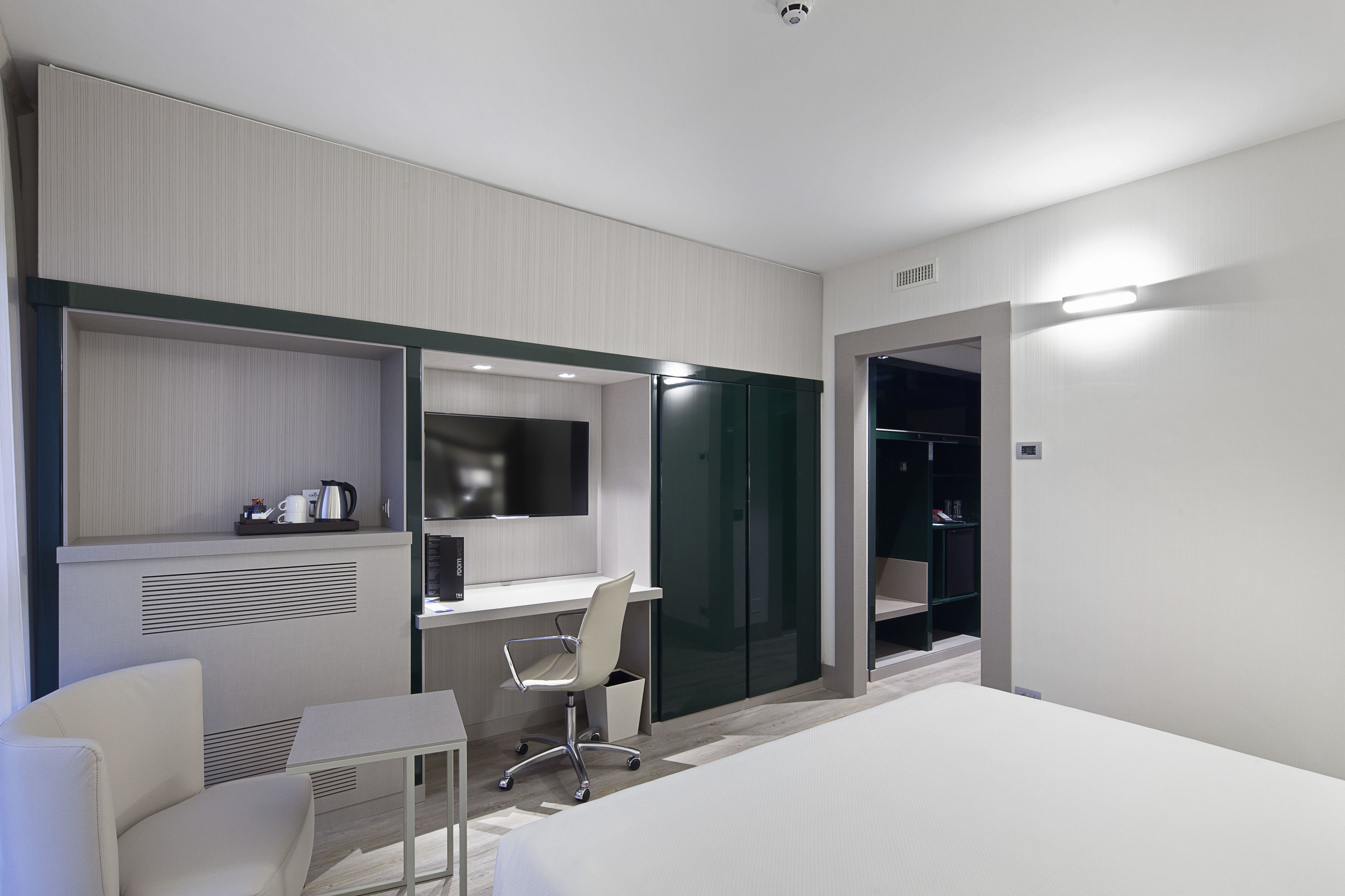 Una habitación de hotel moderna con una cama, un escritorio, una silla, un armario y una mesita con una tetera.