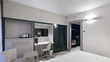 Quarto de hotel moderno com uma cama, uma escrivaninha, uma cadeira, um guarda-roupa e uma pequena mesa com chaleira.