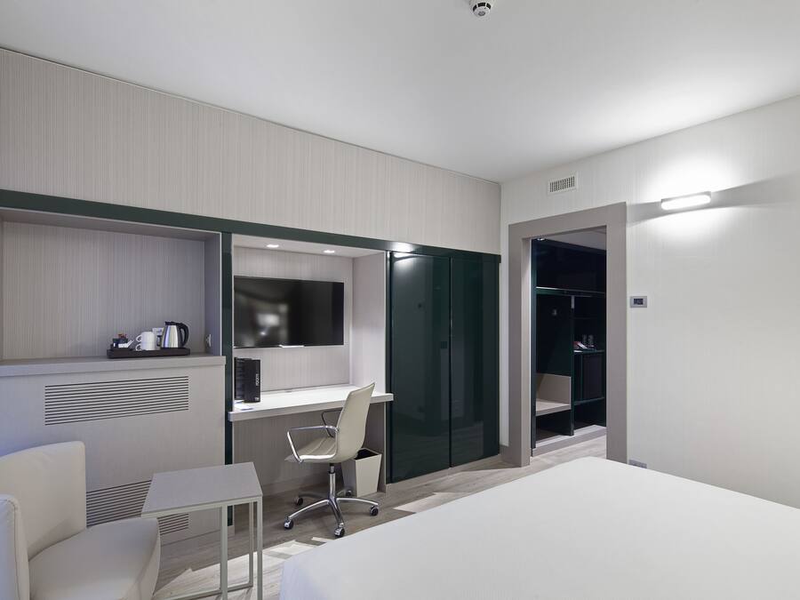 Una habitación de hotel moderna con una cama, un escritorio, una silla, un armario y una mesita con una tetera.