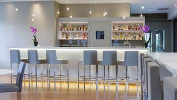 Uma área de bar moderna com bancada branca, banquetas e prateleiras cheias de garrafas.