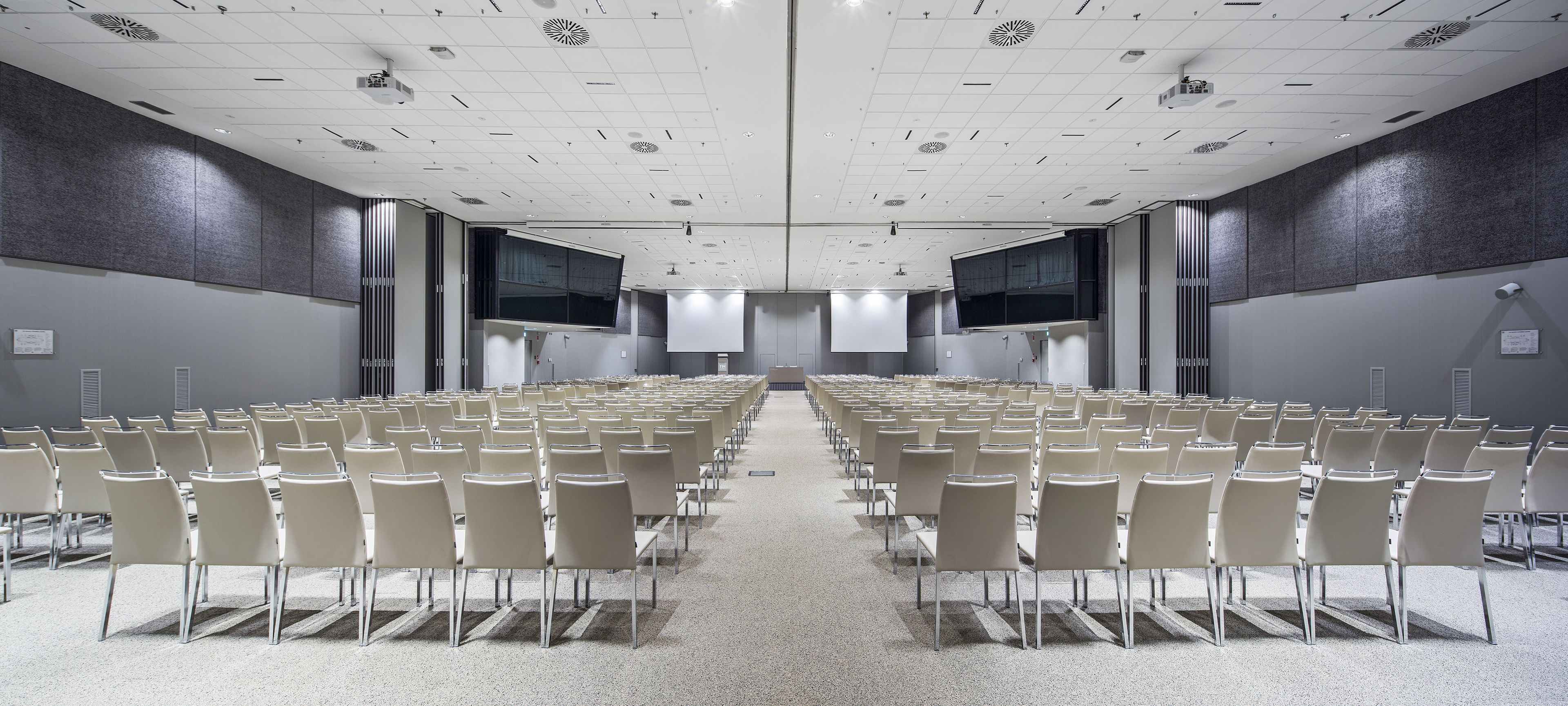 Un salón de conferencias con filas de sillas, una pantalla grande y un proyector.