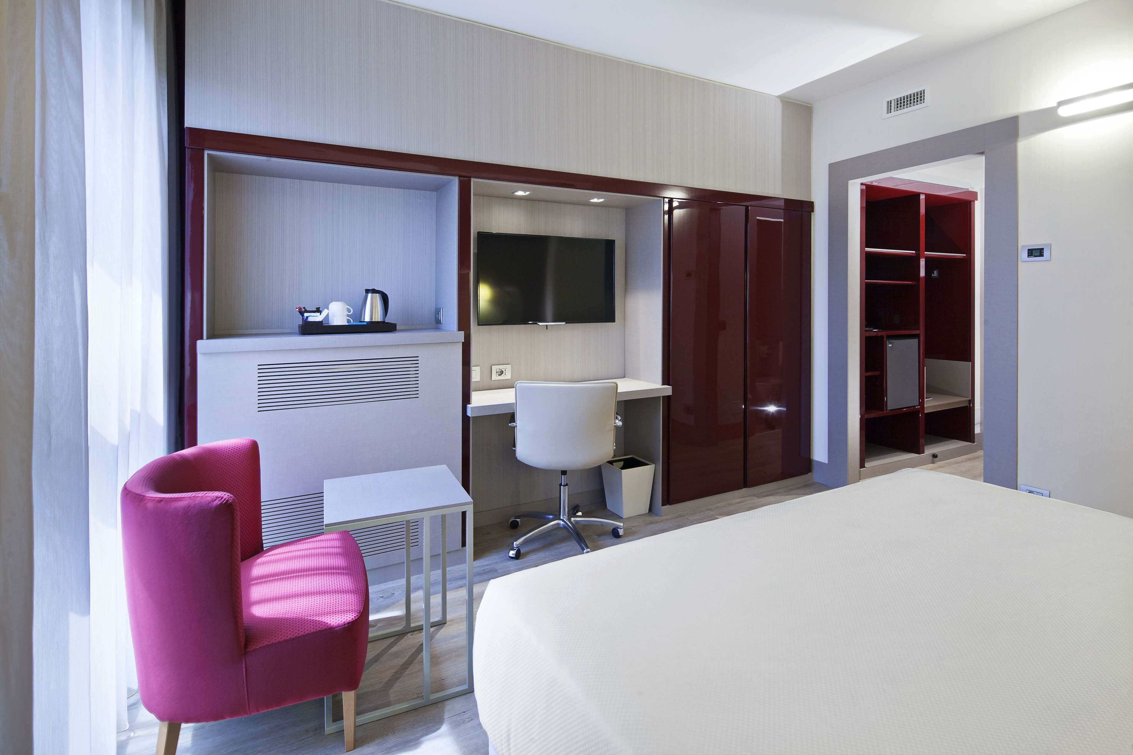 Habitación de hotel con cama, escritorio, silla, televisor y armario.