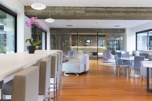 A modern hotel lobby with a wooden floor, white bar area, and seating arrangements. - NH Milano Congress Centre (Assago)