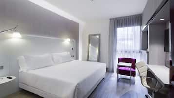 A modern hotel room with a large bed, a desk, a chair, and a TV.