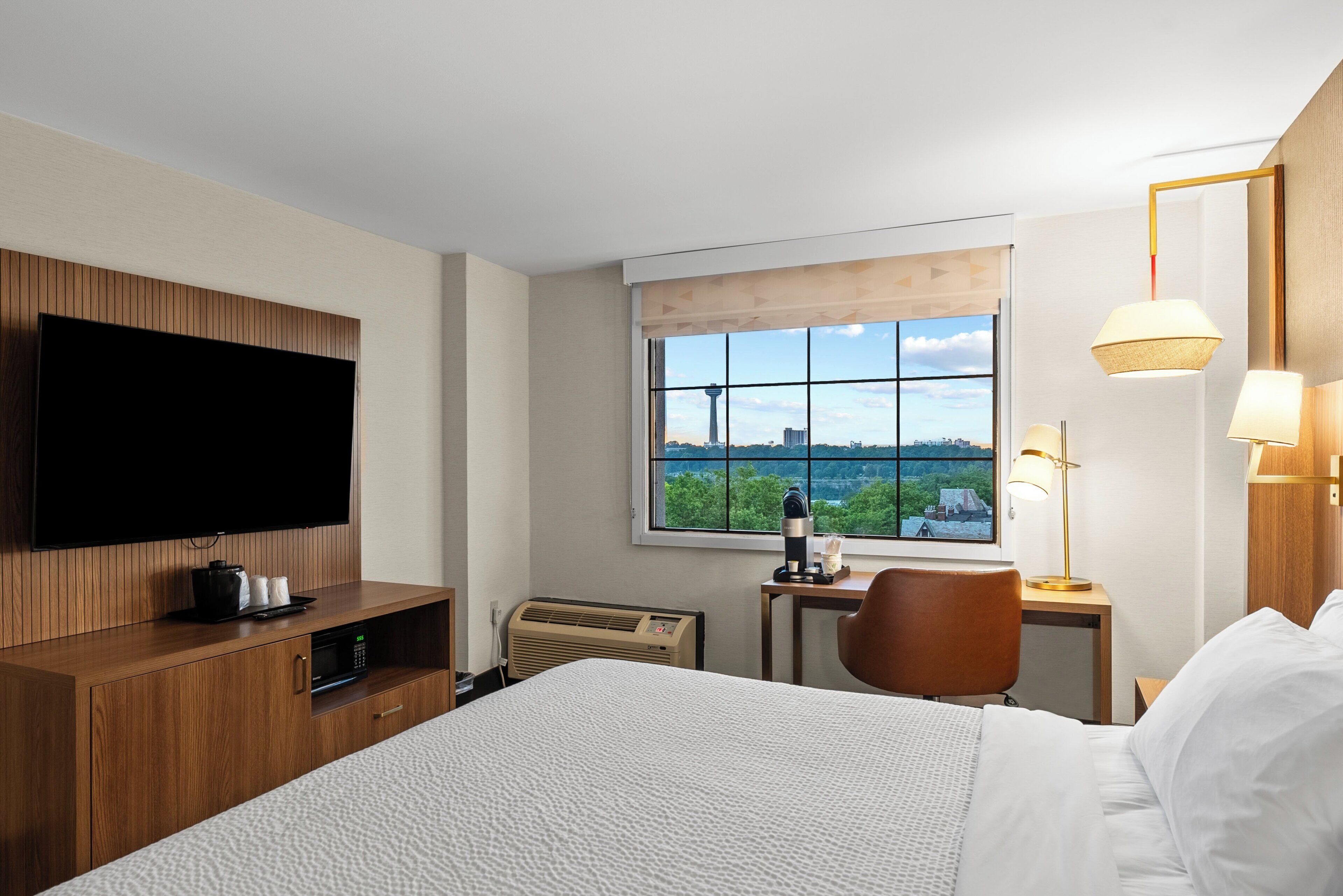 A hotel room with a bed, a desk, a chair, a television, and a window with a city view.