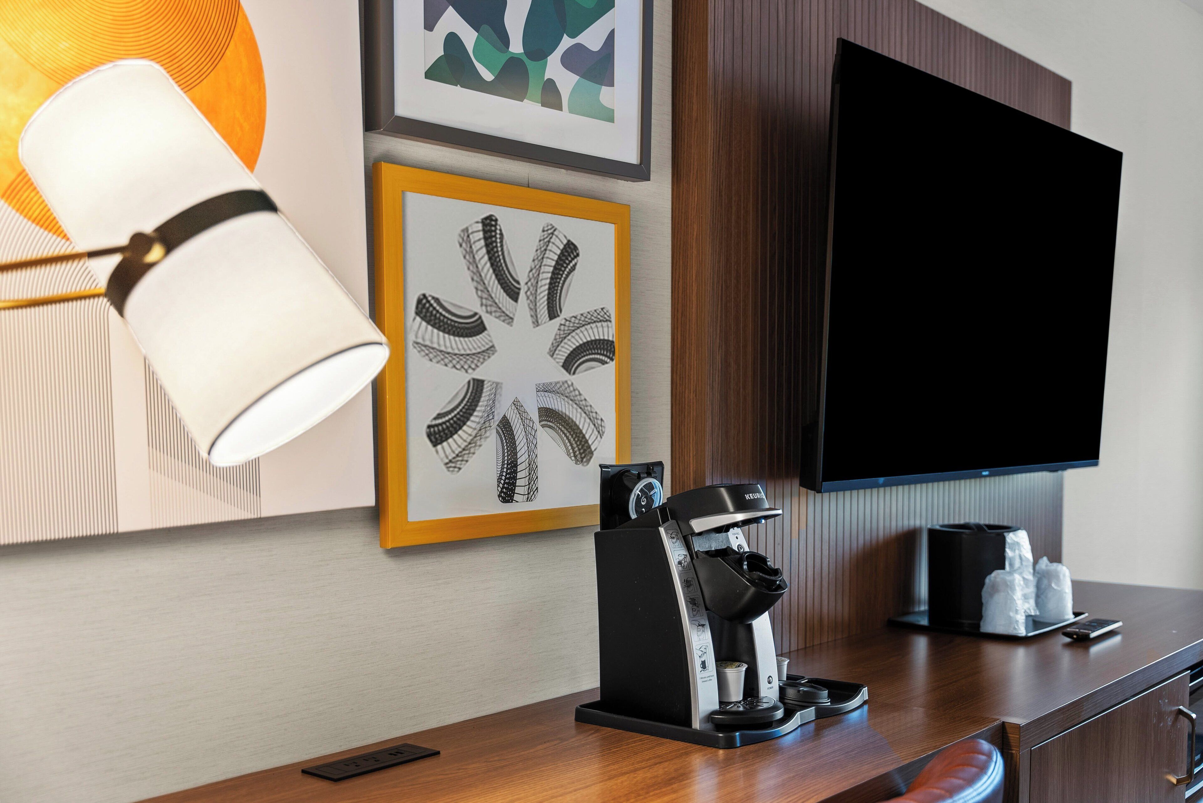 Zona de recepción de un hotel con una máquina de café, un televisor y obras de arte enmarcadas en la pared.