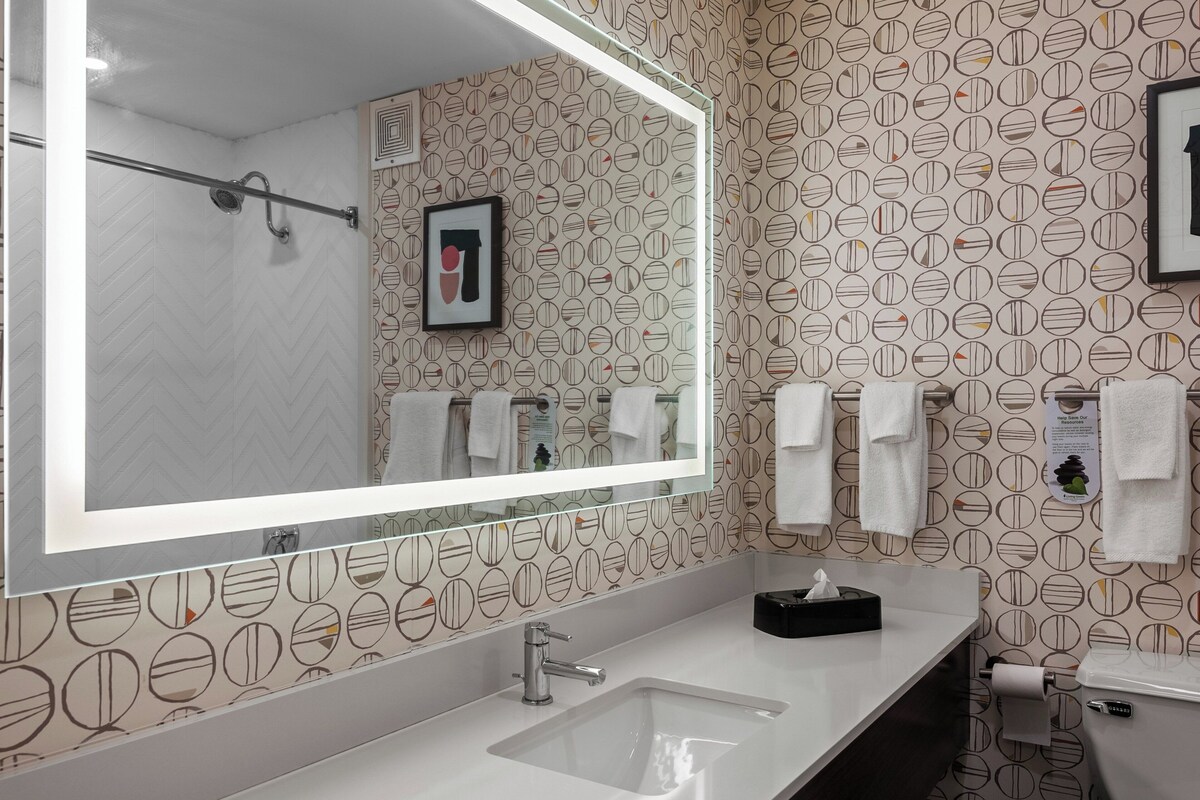 A modern bathroom with a large mirror, two sinks, and a shower.