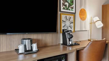 A modern hotel room with a wooden desk, a television, a coffee machine, a microwave, and a leather chair.