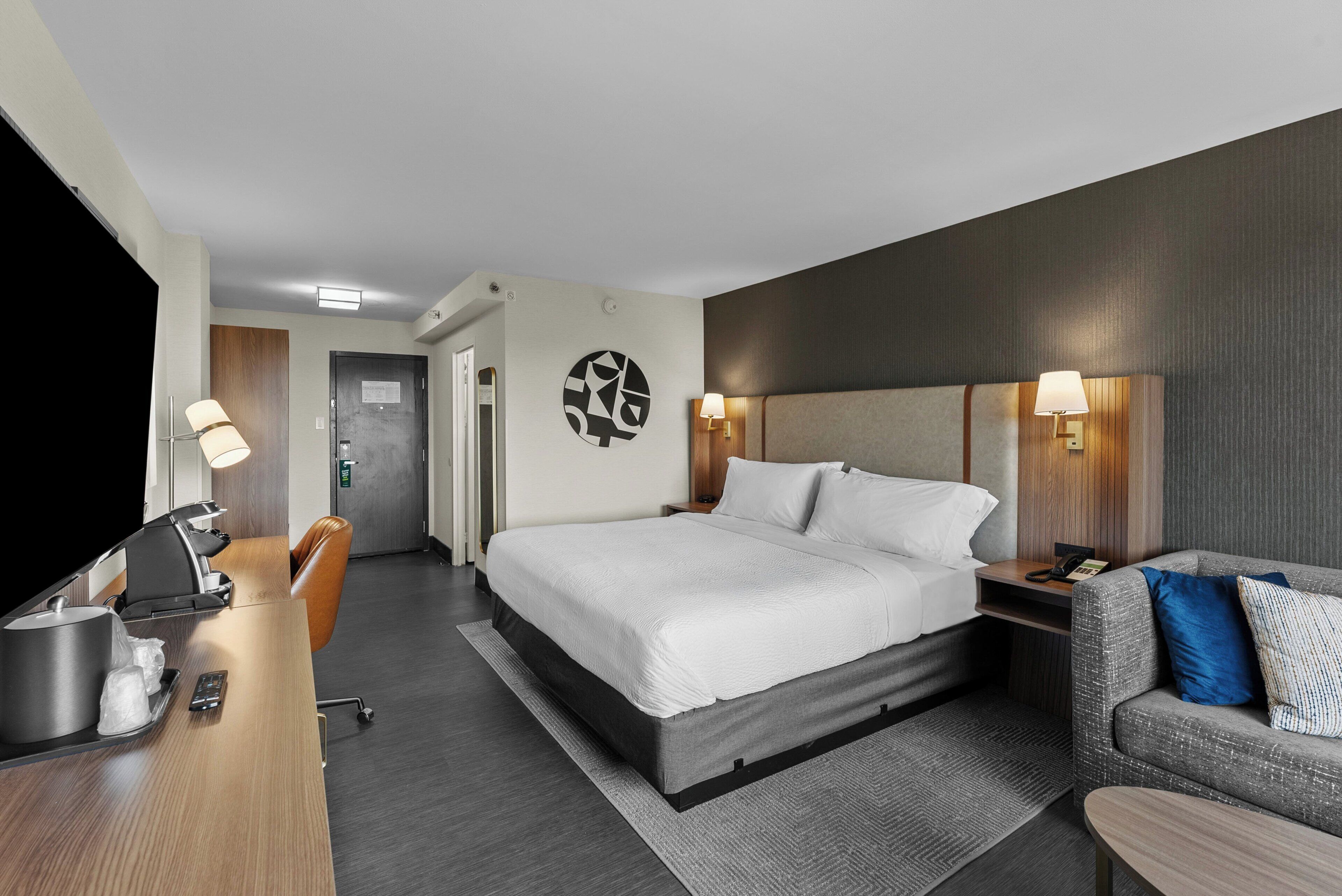 Una habitación de hotel con cama, escritorio, silla, sofá y televisor.