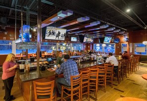 A bar area with multiple seating arrangements, a counter with a bartender, and several televisions displaying sports content. - Holiday Inn Niagara Falls State Park Entry by IHG (Niagara Falls)