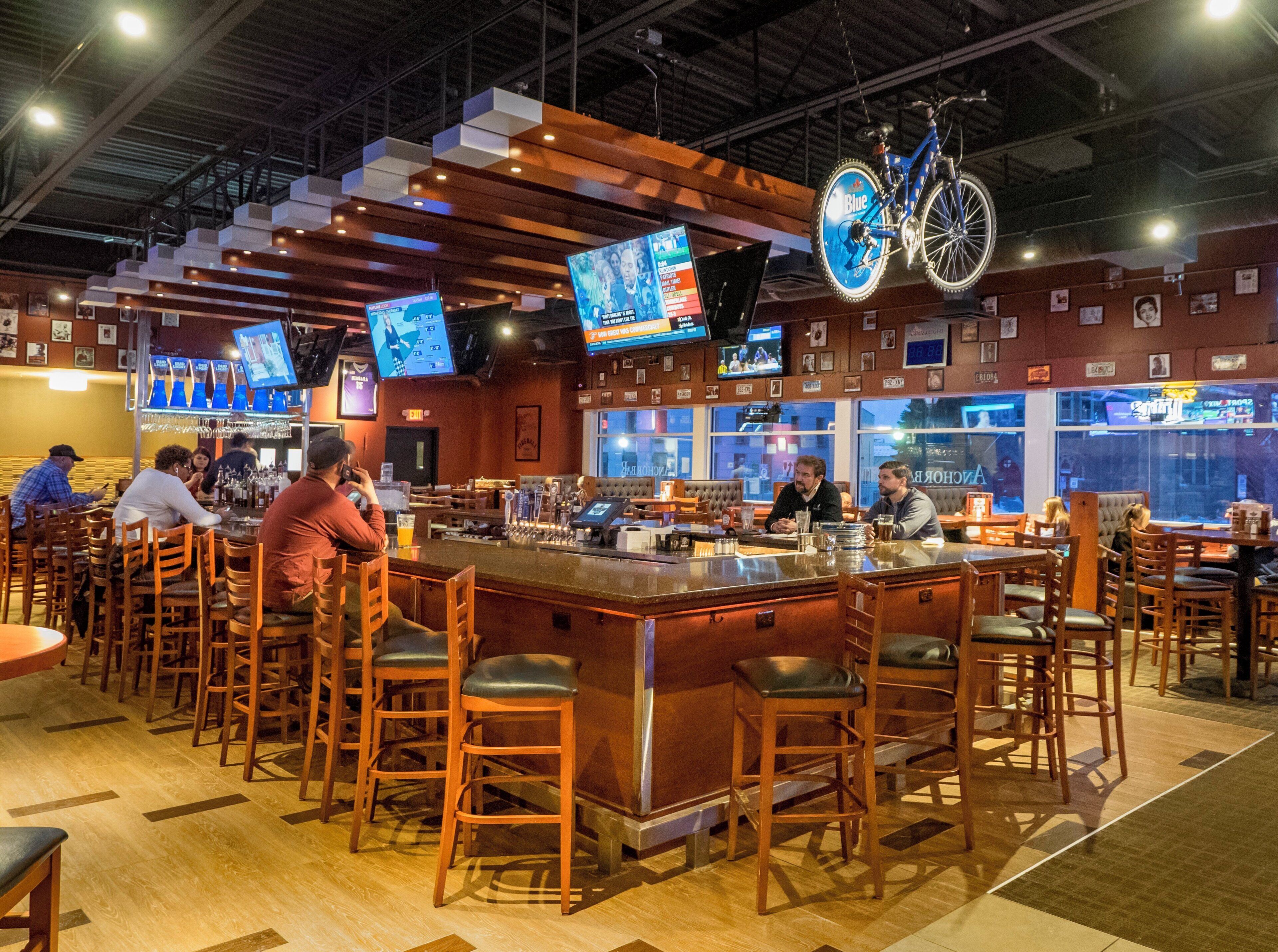 A bar area with wooden stools, a bar counter, and multiple screens displaying content.