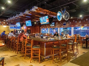 A bar area with wooden stools, a bar counter, and multiple screens displaying content. - Holiday Inn Niagara Falls State Park Entry by IHG (Niagara Falls)