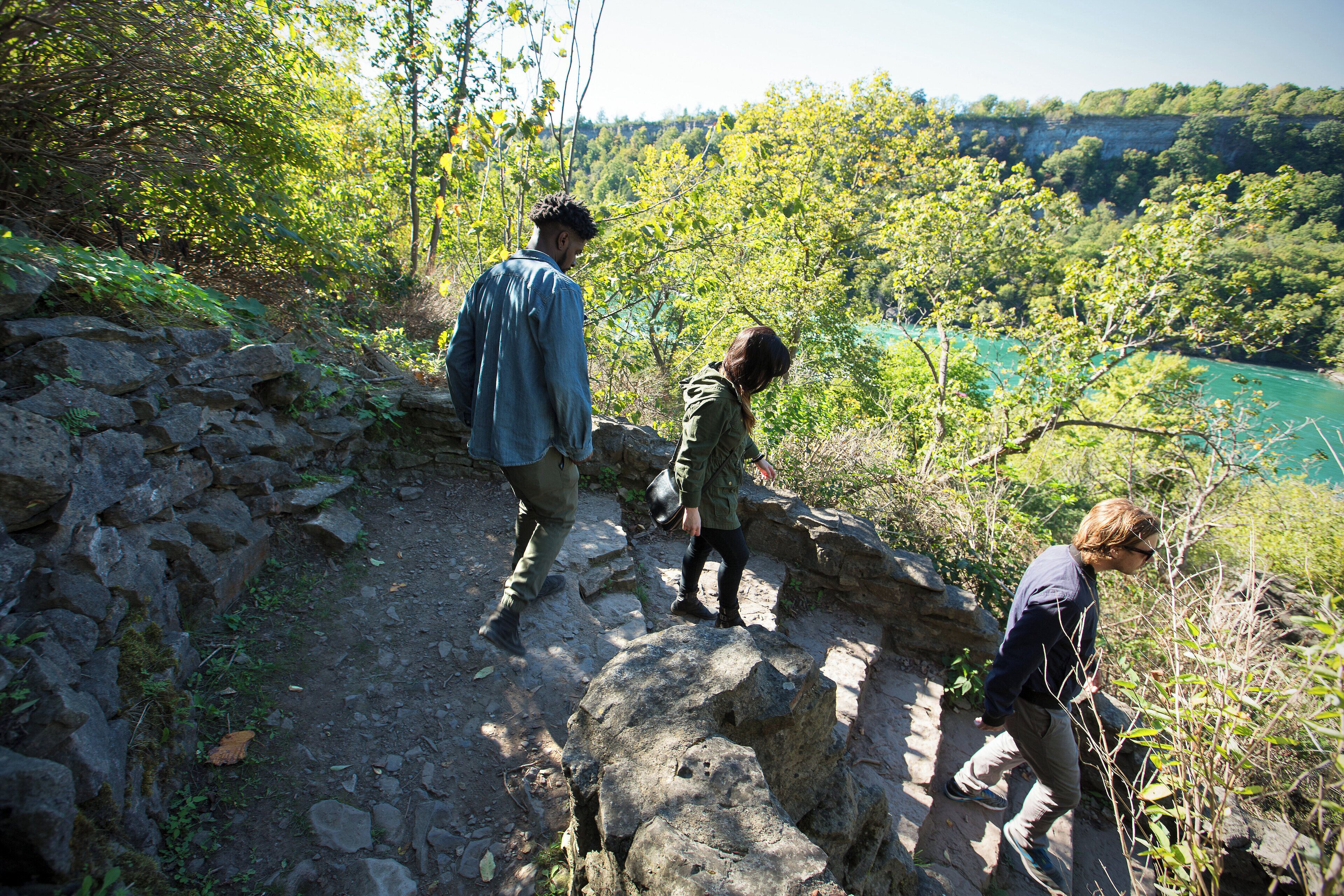 A rocky hiking trail with a view of a river and forest.
