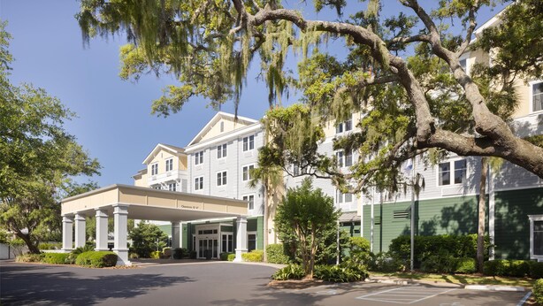 A hotel with a covered entrance, large trees with Spanish moss, and a parking lot.