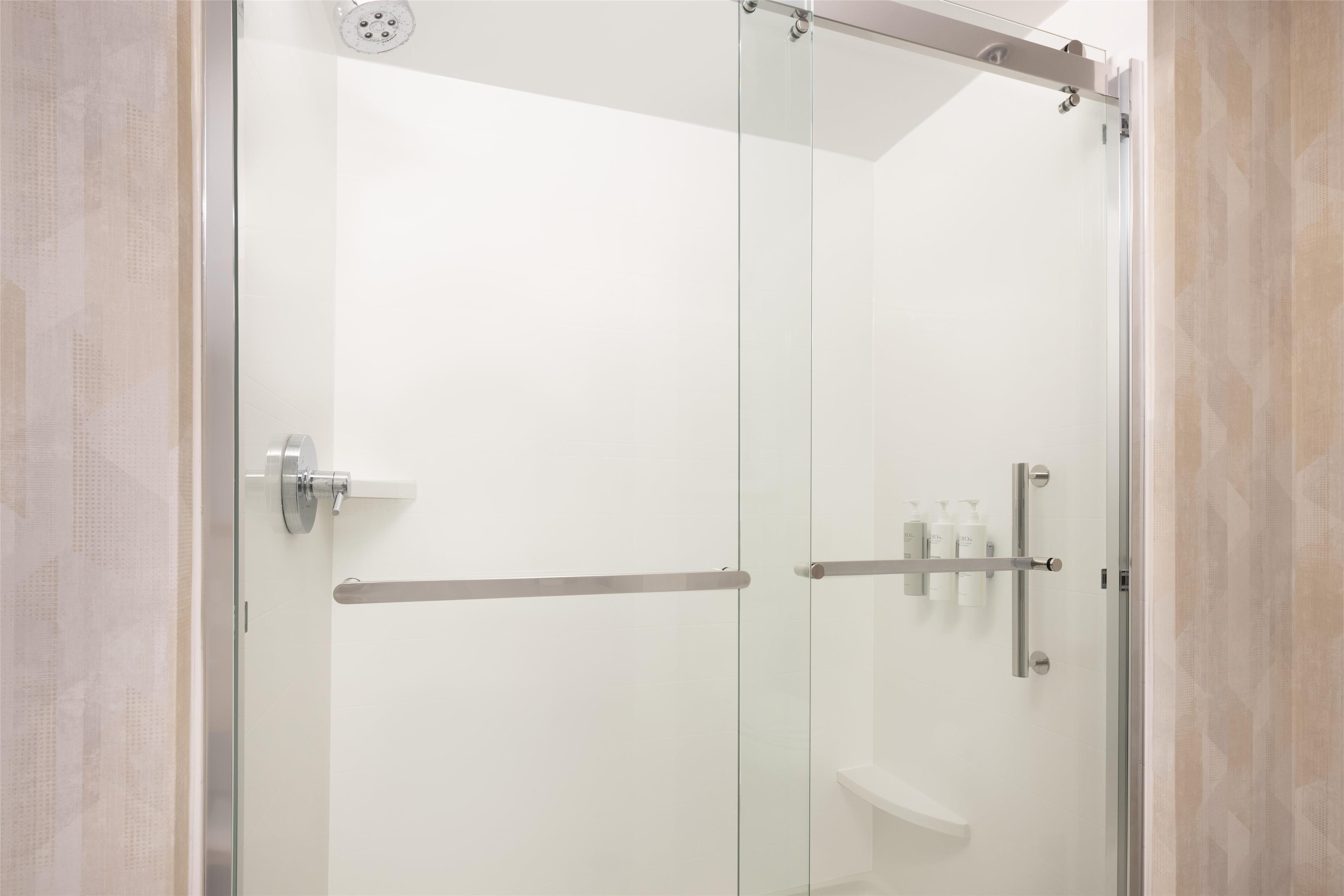 A modern bathroom with a glass shower enclosure, a white sink, and a shelf with toiletries.