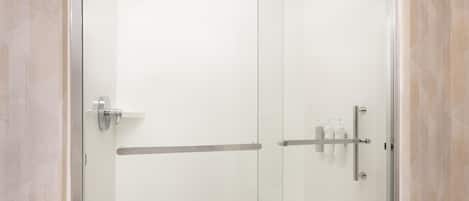 A modern bathroom with a glass shower enclosure, a white sink, and a shelf with toiletries.