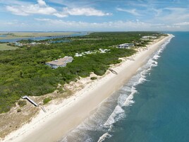 An aerial view of a coastal area with a beach, a bridge, and several buildings.
