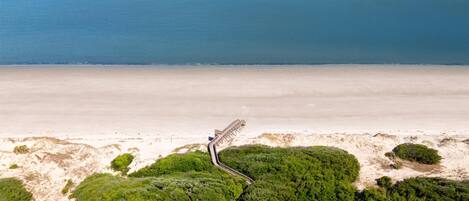 Vue aérienne d’une plage avec une promenade en bois menant à un abri de plage.
