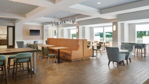 A spacious dining area with wooden flooring, a central seating area with a sofa and chairs, and large windows providing natural light.