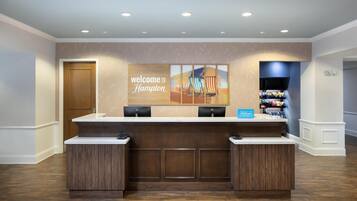 A hotel reception desk with a "Welcome to Hampton" sign, a counter, and a display of amenities.