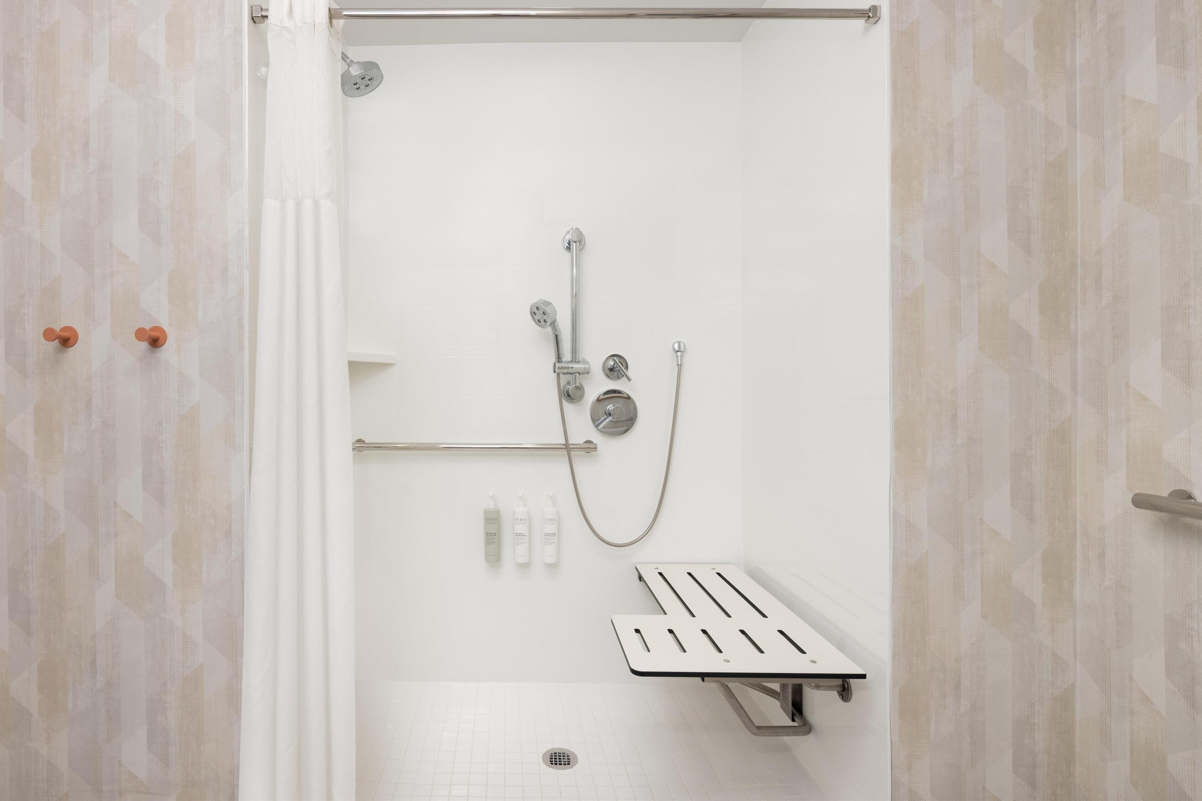 A modern shower area with a handheld showerhead, a wall-mounted faucet, and a handheld showerhead. There are three bottles of shampoo and conditioner on the wall.