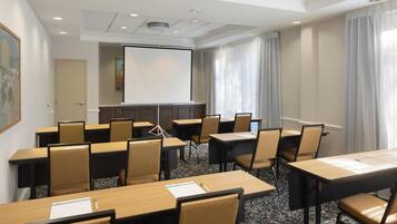 Un salón de conferencias con varias mesas y sillas, una pantalla de proyector y un amplio ventanal con cortinas.