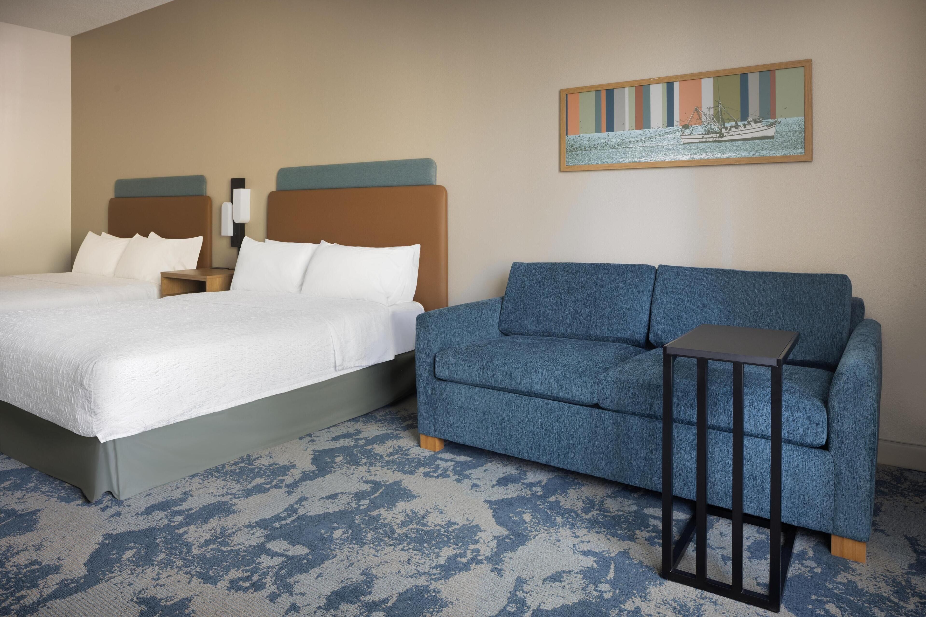 Ein Hotelzimmer mit einem Bett, einem blauen Sofa, einem kleinen Tisch und einem Bild an der Wand.