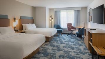 A hotel room with two beds, a desk, a chair, a TV, and a window with curtains.