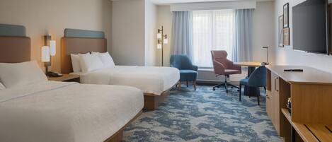 Habitación de hotel con dos camas, un escritorio, una silla, un televisor y una ventana con cortinas.