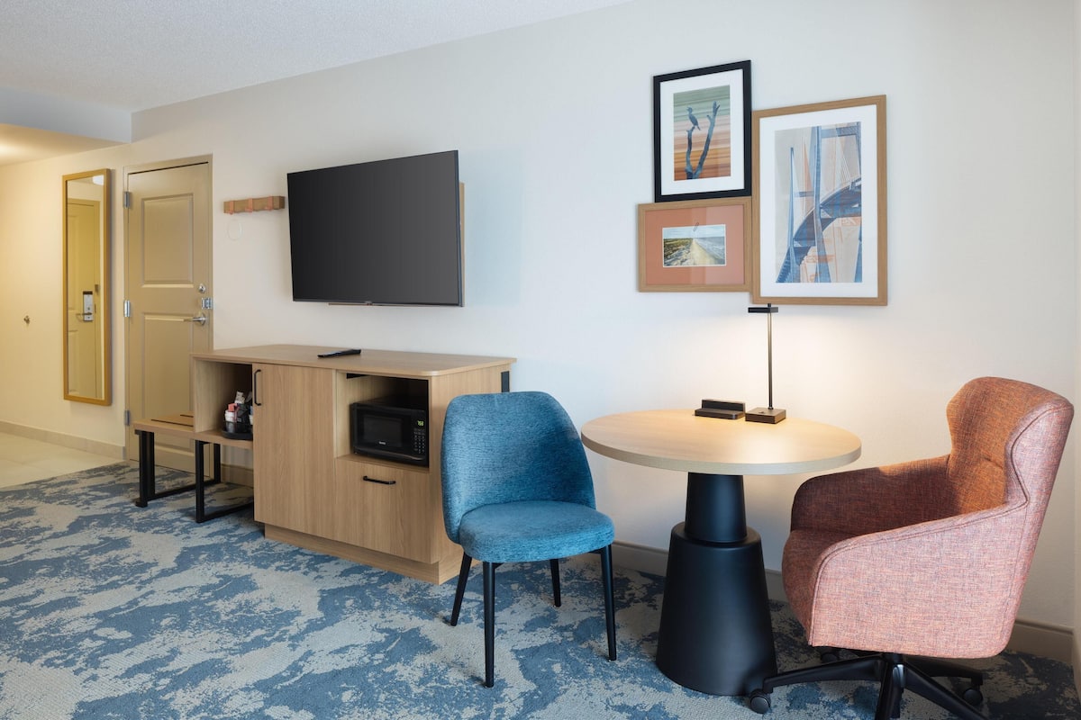 A hotel room with a TV, two chairs, a small table, a microwave, and a cabinet.