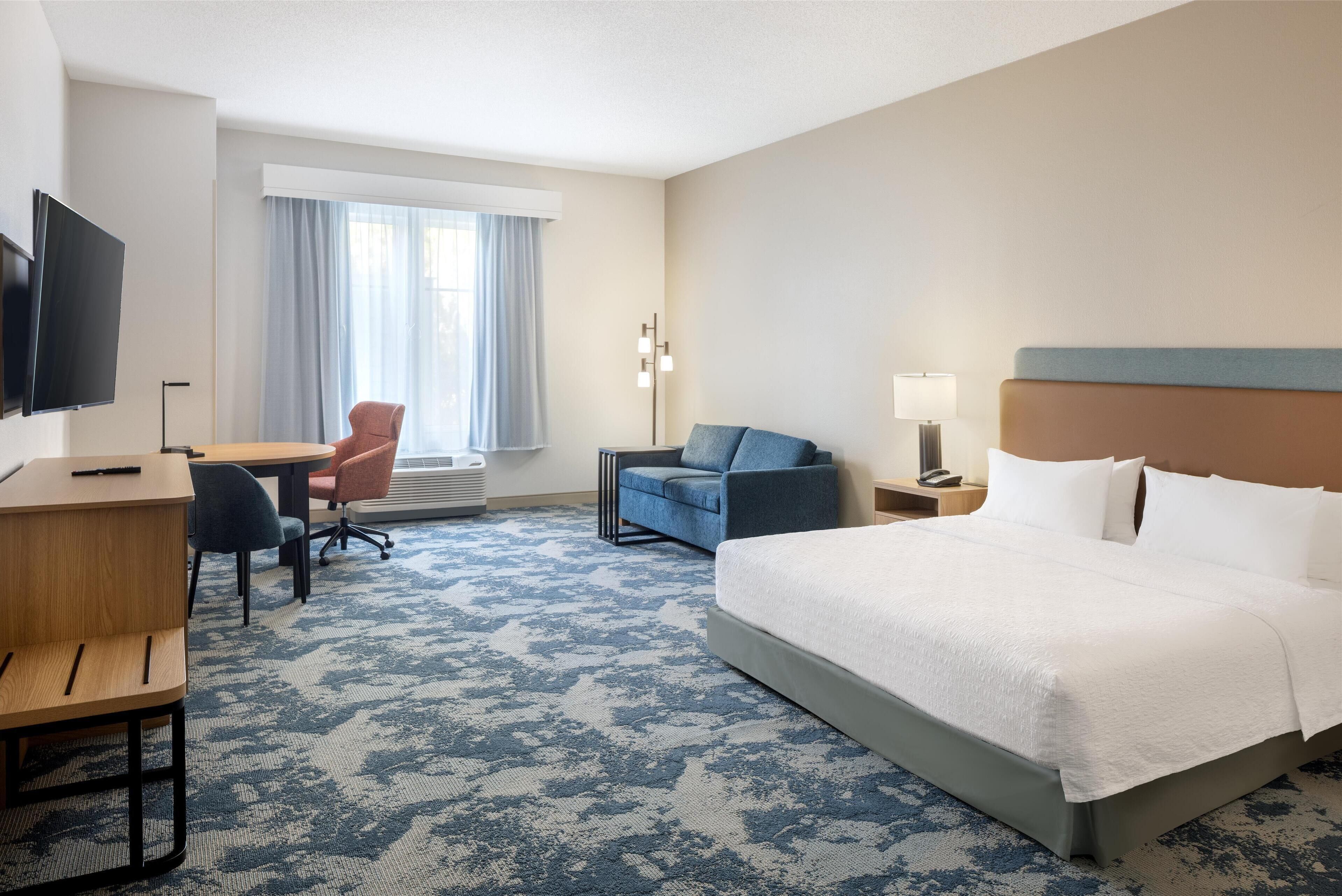 A hotel room with a large bed, a desk with a chair, a TV, and a window with curtains.
